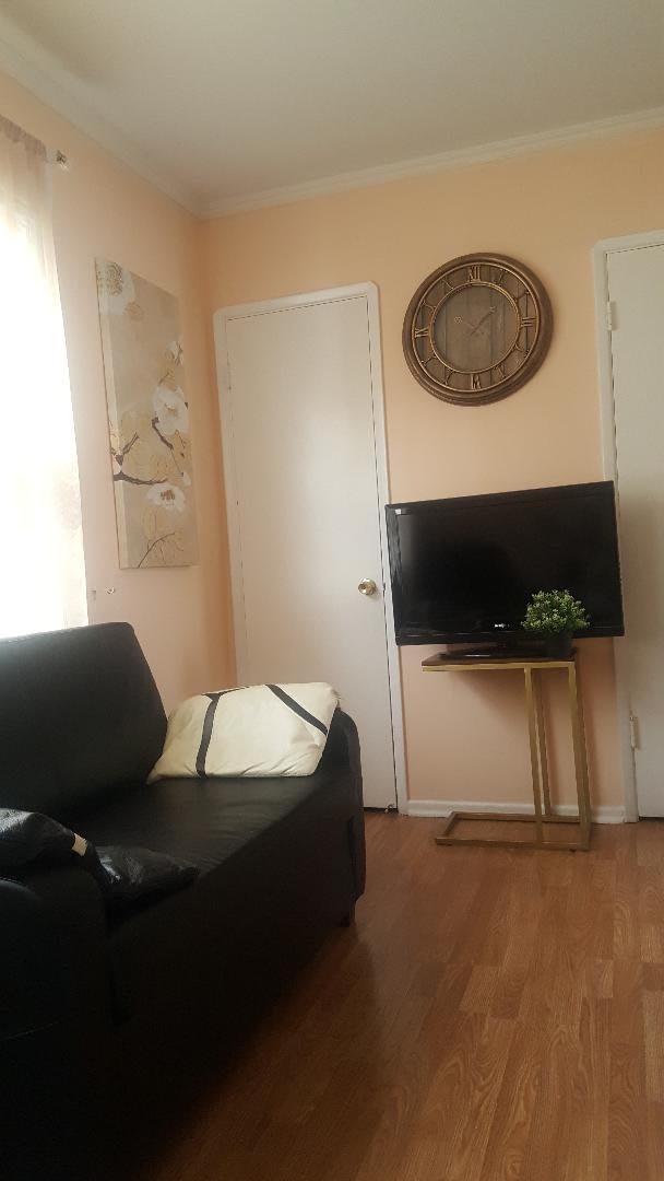 A cozy and modern living room with a black sofa, a television on a stand, wall art, and ample natural light.