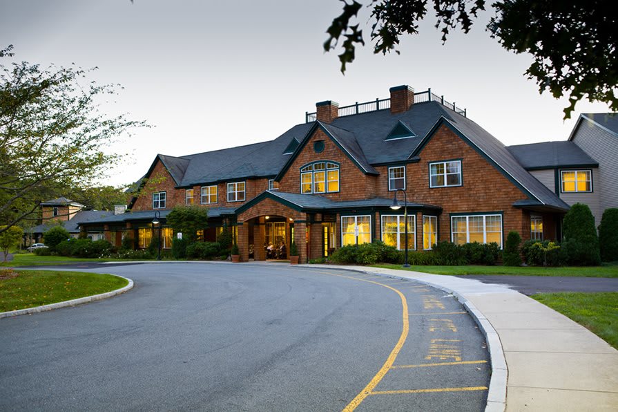 A charming brick hotel with a circular driveway, set against an evening sky.