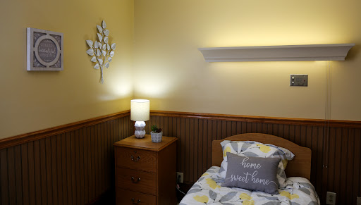 A cozy and well-decorated bedroom with yellow walls, featuring a nightstand with a lamp and decorative bedding.