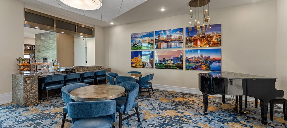 A modern lounge area featuring round tables, blue chairs, vibrant artwork on the wall, and decorative lighting.