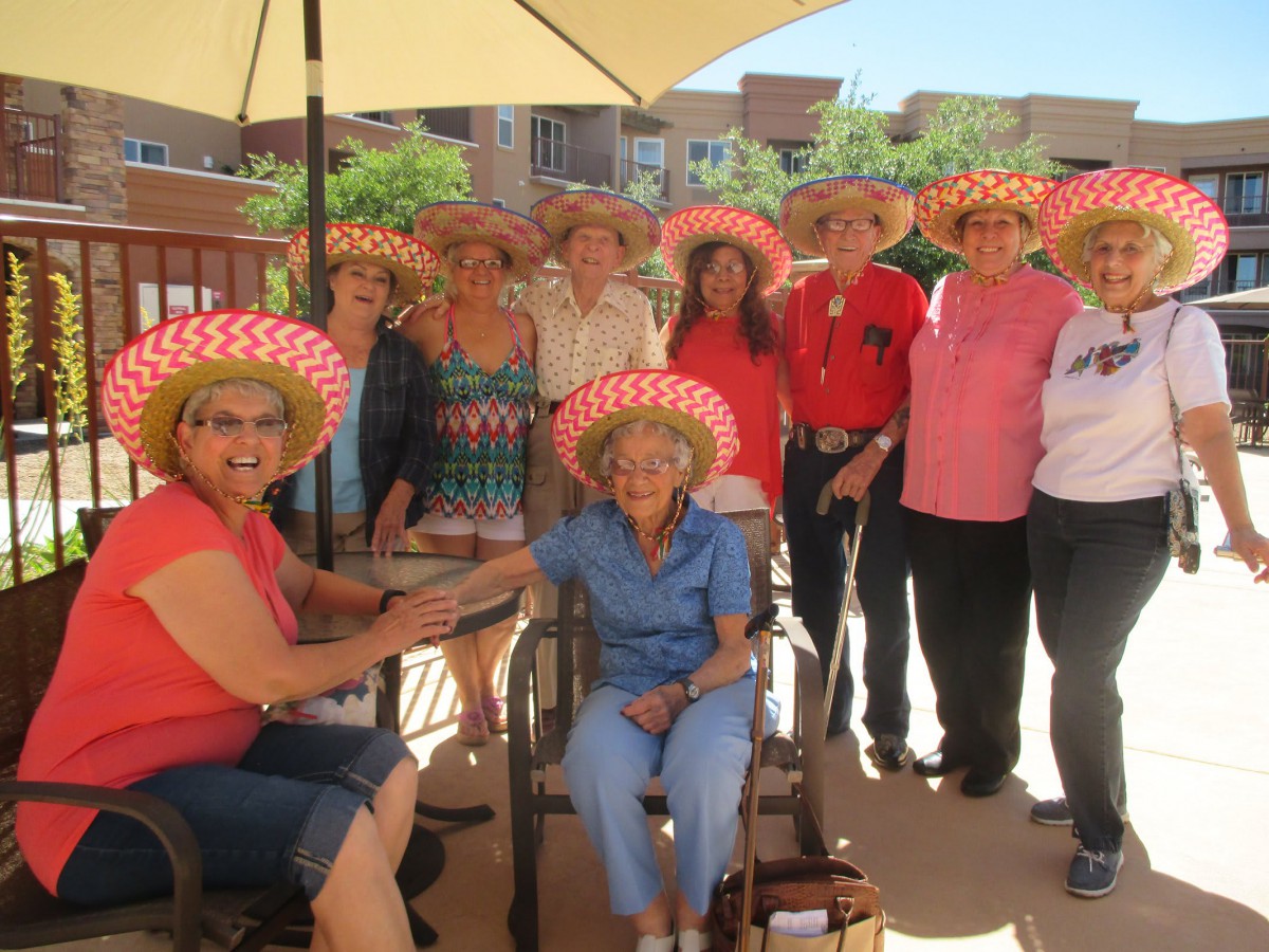 A group of people wearing hats gathered outdoors, smiling and enjoying a sunny day.