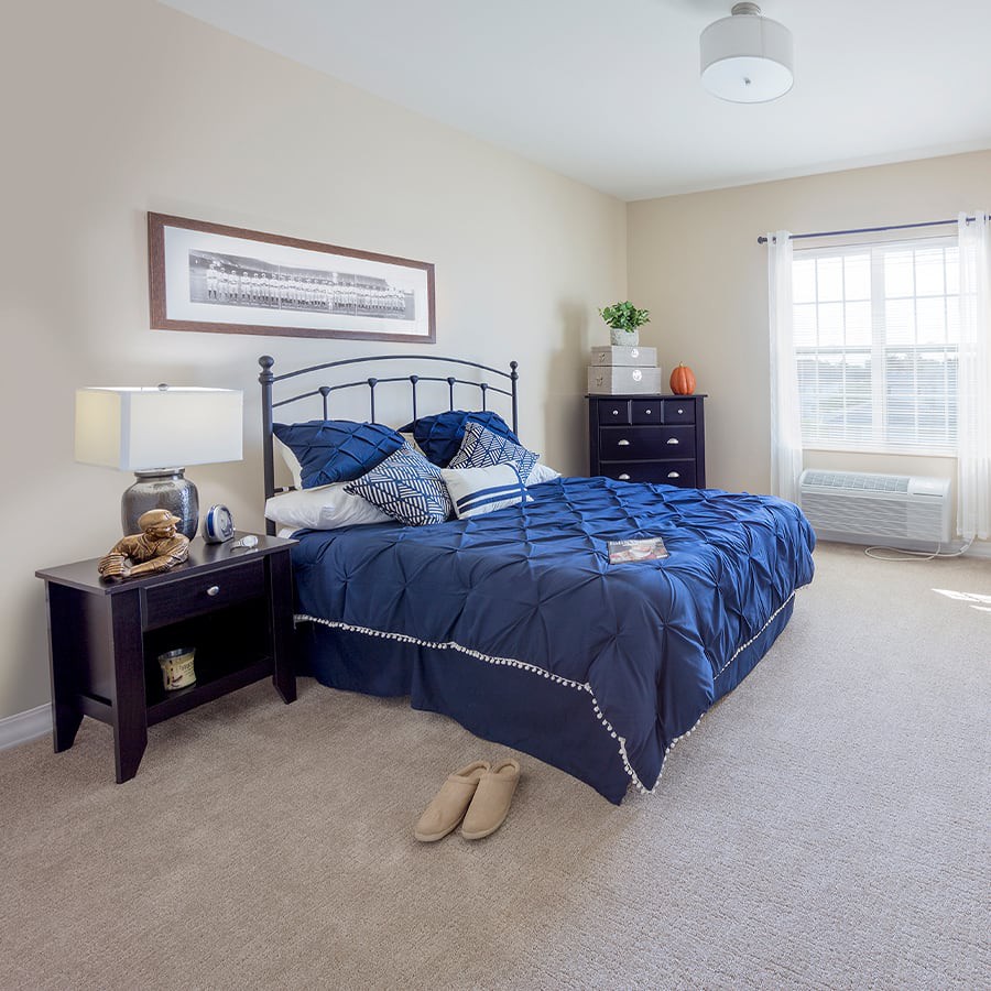 A cozy and well-decorated bedroom with a blue bedspread, nightstands, and large windows.