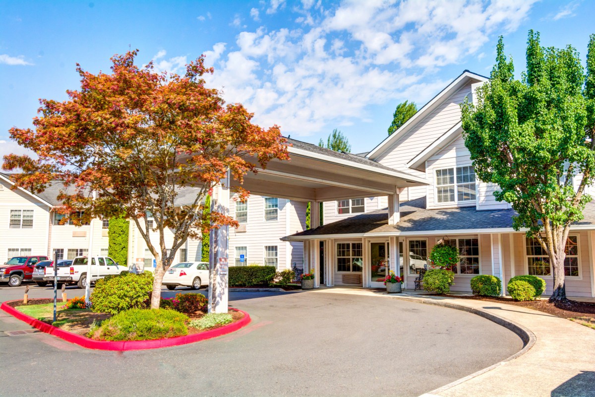 A modern hotel entrance with a landscaped driveway and trees.