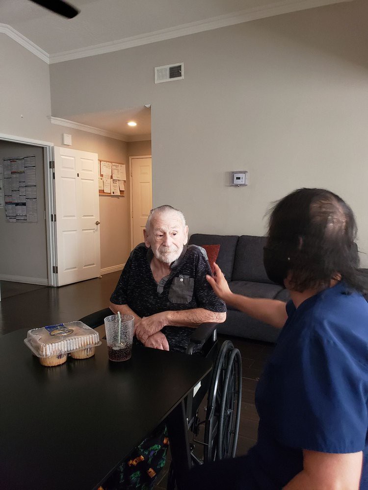 An older adult in a wheelchair is being assisted by a caregiver during mealtime.