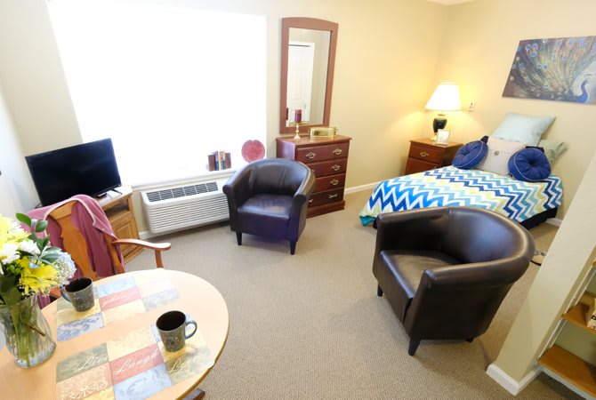 A cozy bedroom with seating area, featuring a bed, chairs, table, and lamp.