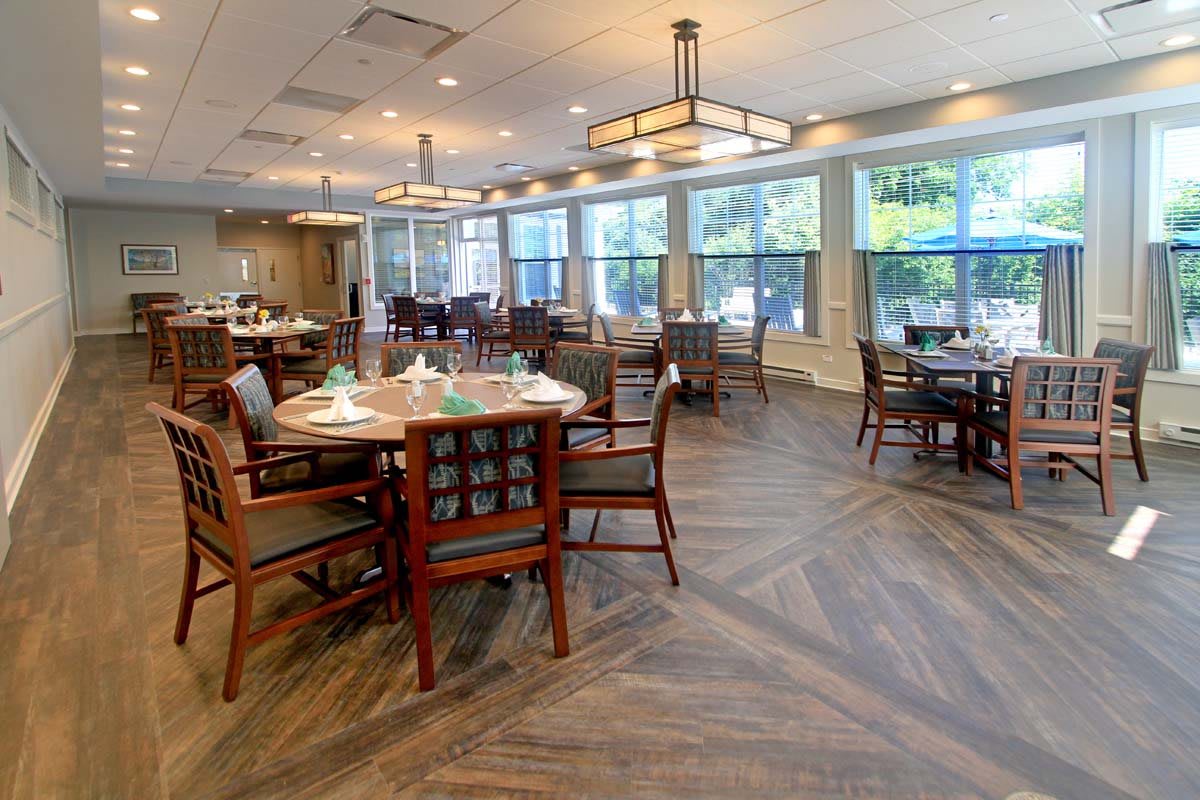 A well-arranged dining area with tables and chairs, featuring large windows and elegant lighting.