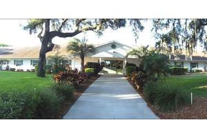 A beautifully landscaped entrance pathway leading to a building, surrounded by lush greenery and palm trees.