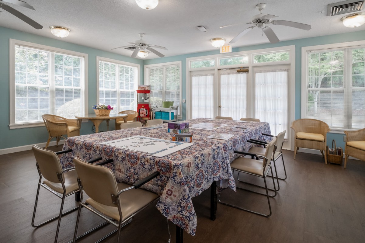 A well-lit craft room with tables and chairs set up for activities, surrounded by large windows.