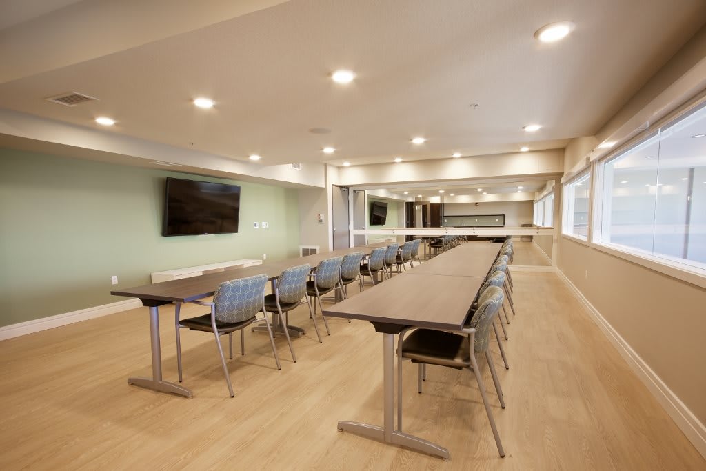 A modern conference room with long tables and chairs, equipped with a large screen.