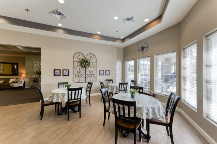 A well-lit dining area featuring multiple tables and chairs, decorated with wall art and large windows.