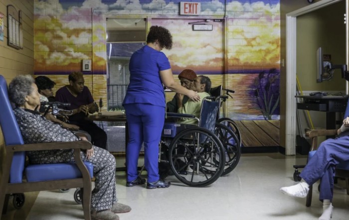 A healthcare worker assists an elderly person in a wheelchair in a nursing home setting.