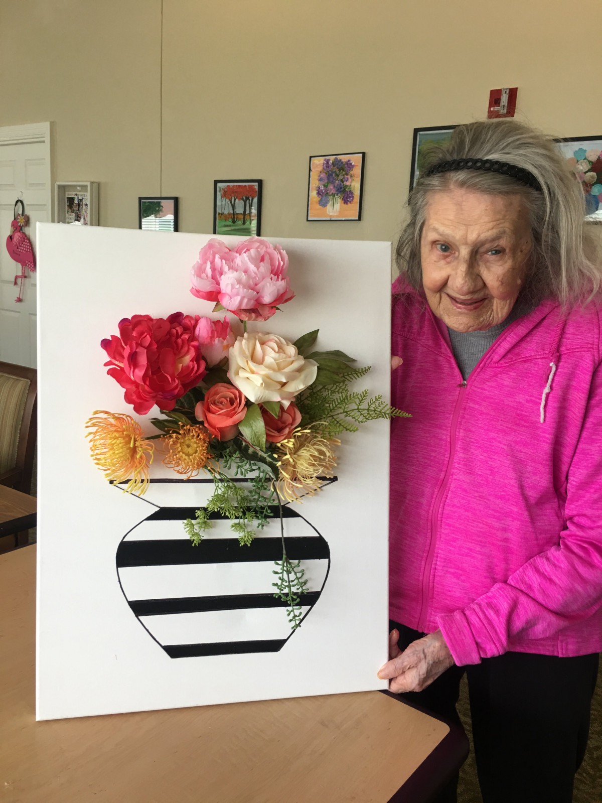 A woman holding a floral artwork featuring colorful flowers arranged in a striped vase.