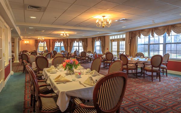 An elegantly decorated dining room with neatly arranged tables and chairs, illuminated by chandeliers.
