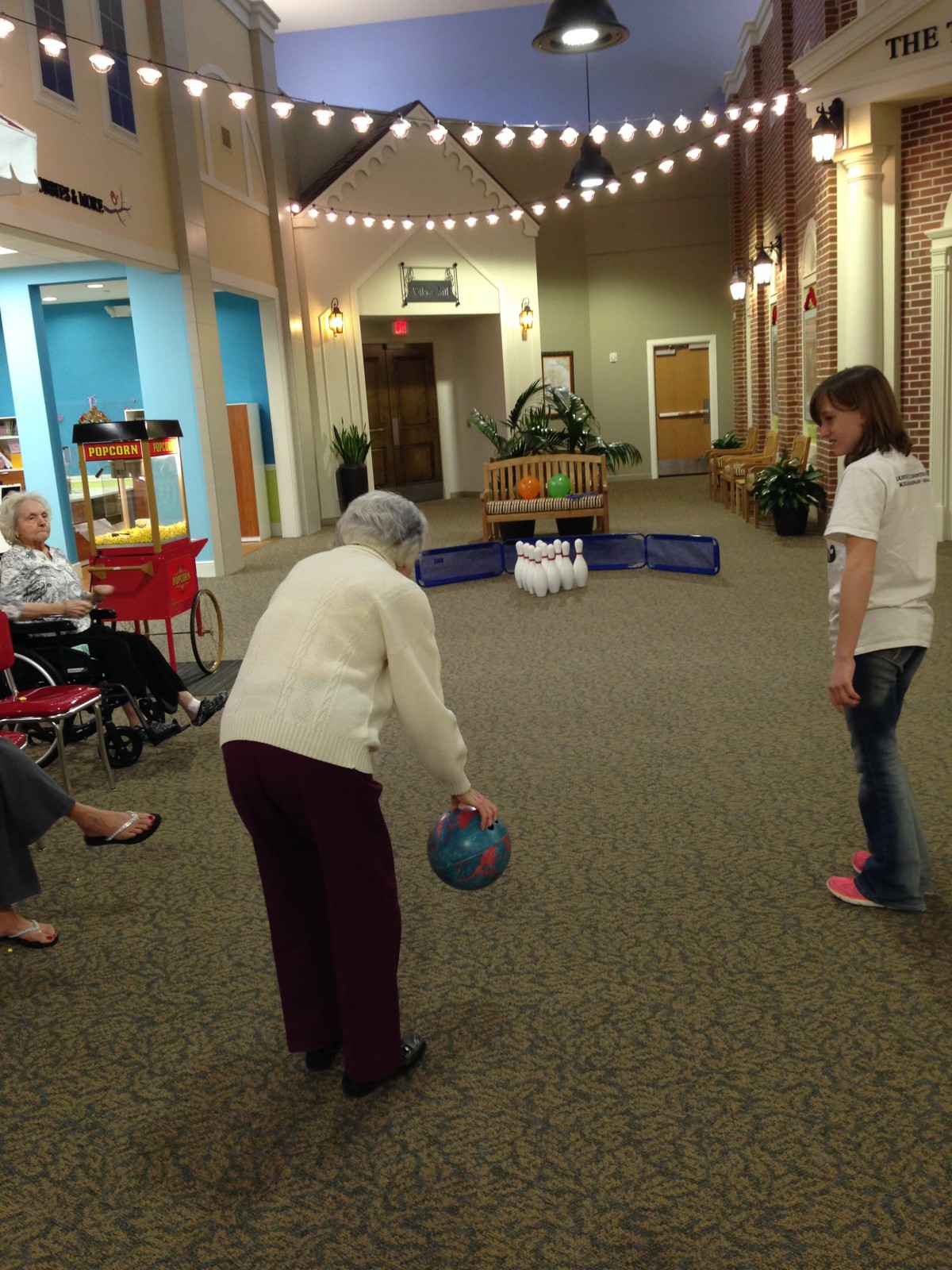 An elderly person participates in an indoor bowling activity at a community center.