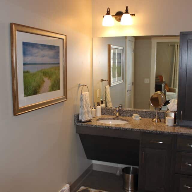 A modern bathroom with a vanity and mirror, featuring a decorative painting on the wall.