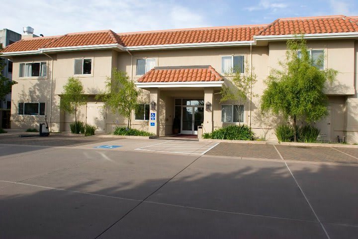 A sunny day view of a two-story building with a red-tiled roof and landscaped entrance.