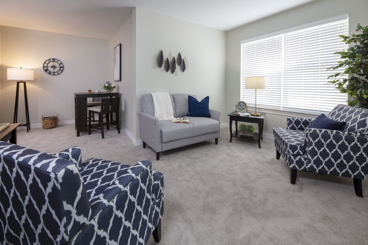 A cozy living room with modern furniture, featuring a sofa, armchairs, and a coffee table under soft natural lighting.