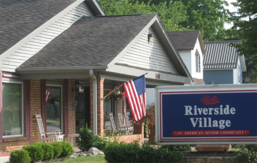 A suburban house with an American flag displayed and a real estate sign in the front yard.