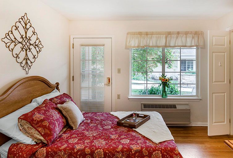 A cozy bedroom with a decorative red bedspread and a window letting in natural light.