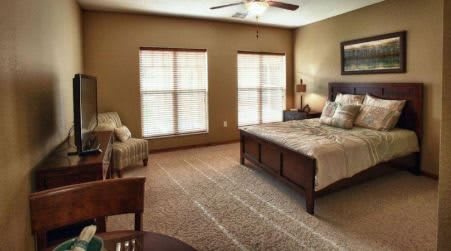 A cozy bedroom with a wooden bed, carpeted floor, and large windows.