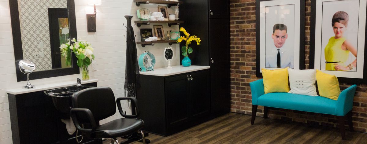A cozy office corner with a black storage cabinet, shelves displaying decor, and a comfortable chair on wooden flooring.
