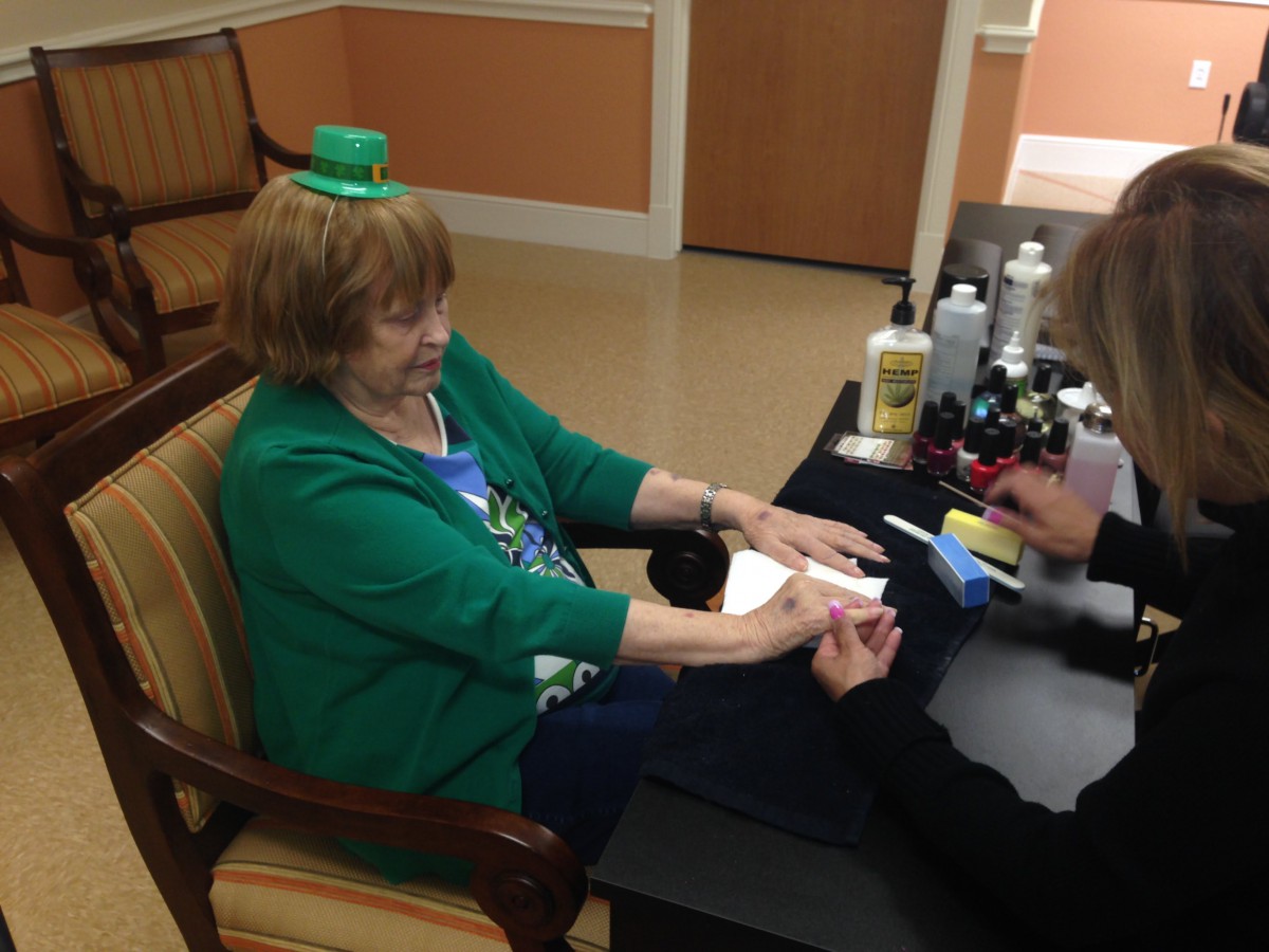 A woman is getting a manicure while wearing a small green hat, celebrating St. Patrick's Day.