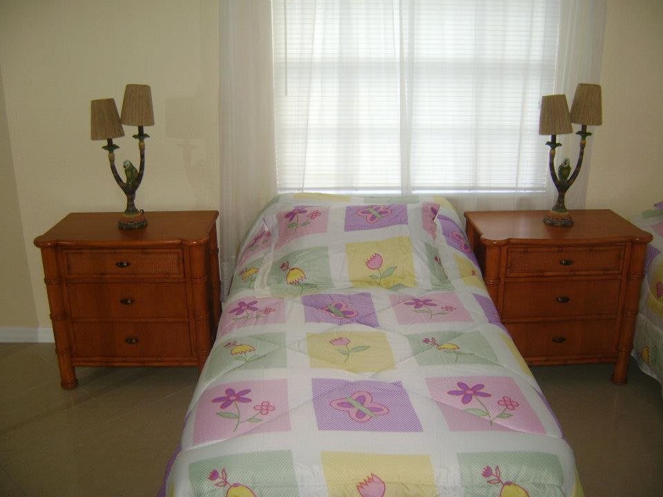 A cozy bedroom with a bed covered in a colorful quilt, flanked by two nightstands and lamps, and a window in the background.