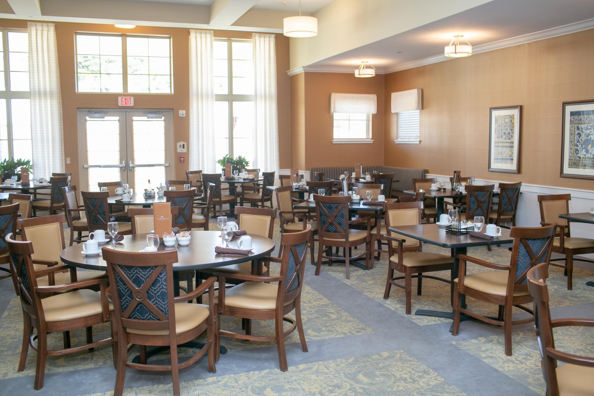 A spacious dining area with neatly arranged tables and chairs, featuring large windows and bright lighting.