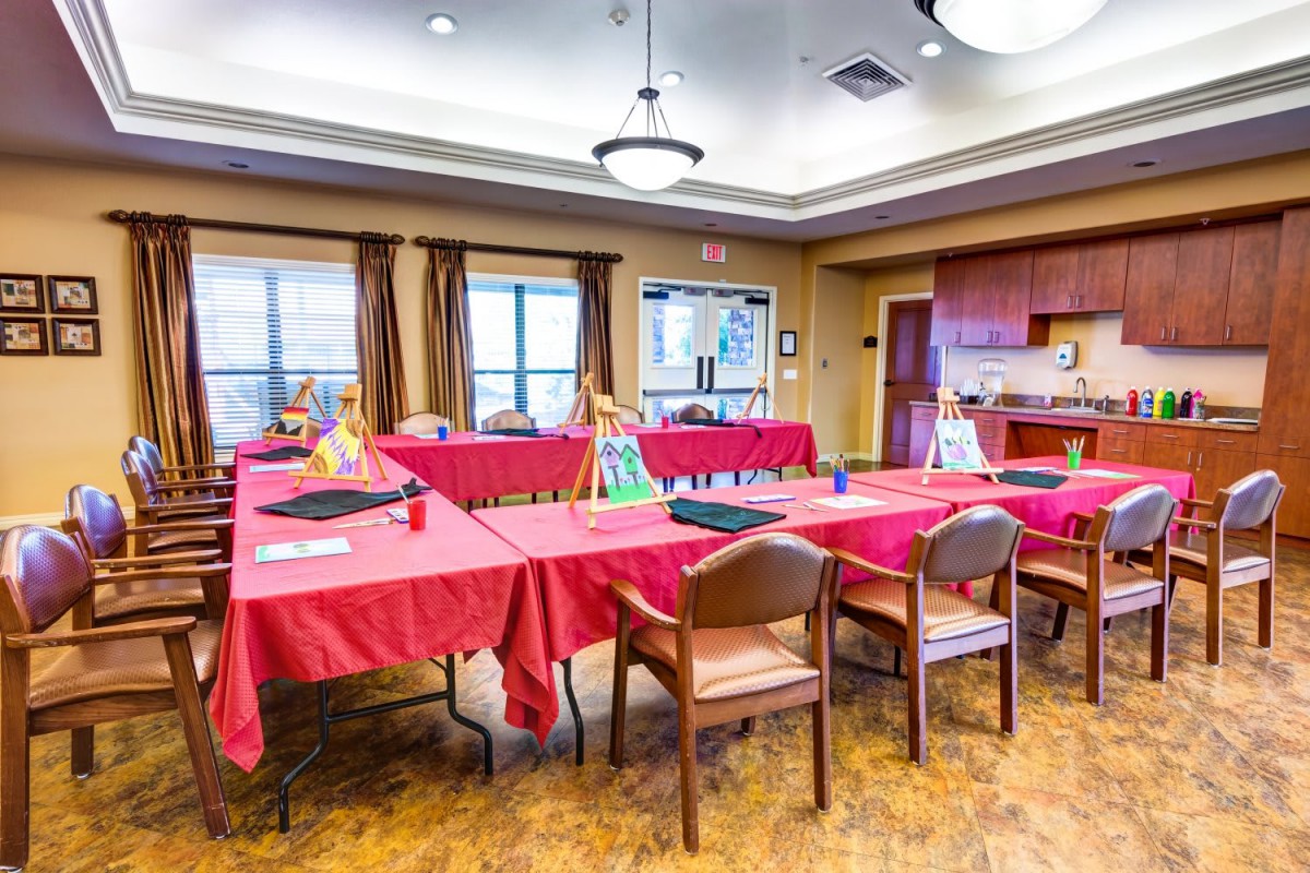 A brightly lit conference room set up for an art class, with tables covered in red tablecloths and painting supplies.
