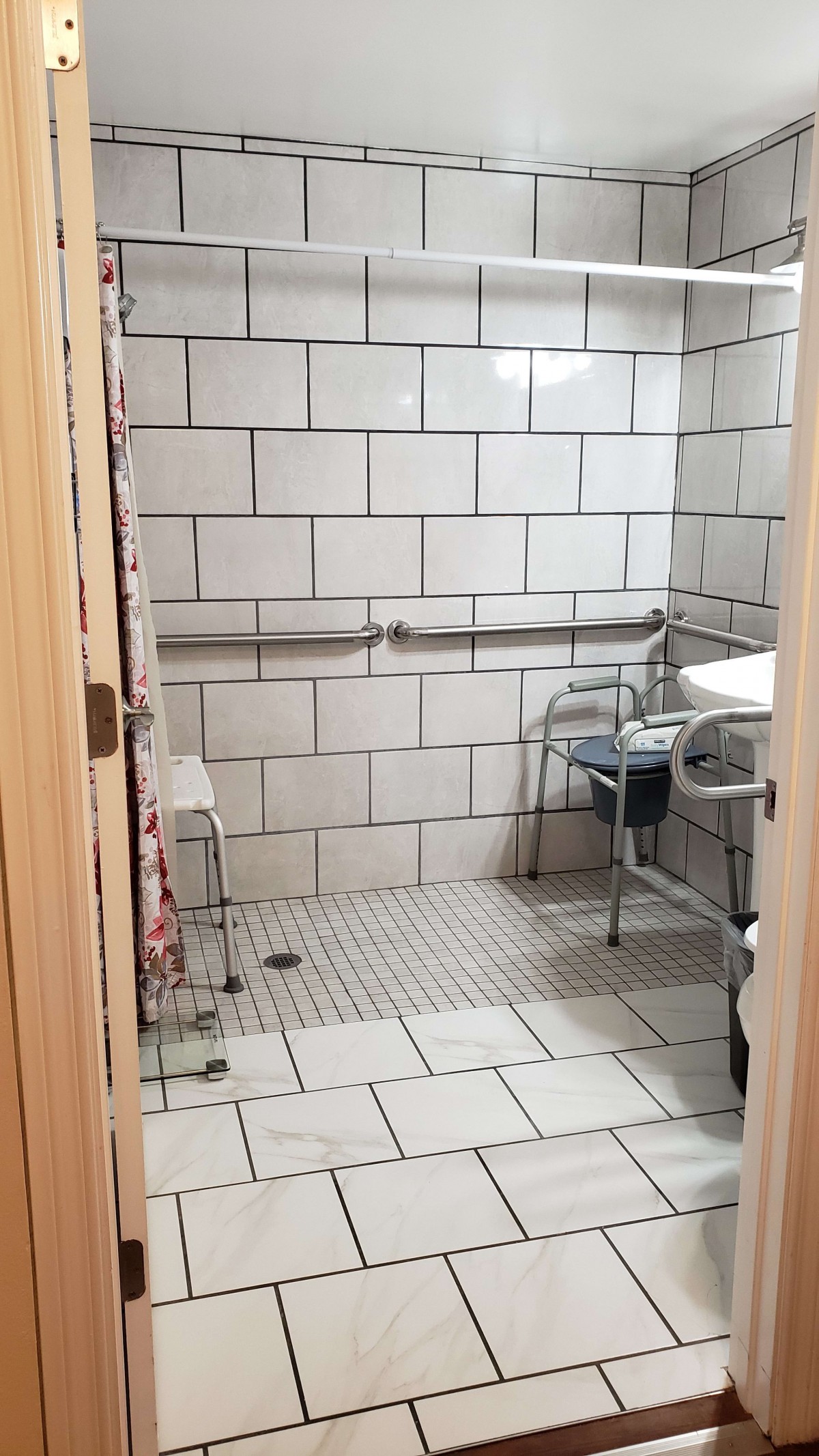 An accessible bathroom with tiled walls and floor, featuring grab bars and a shower chair for increased mobility support.