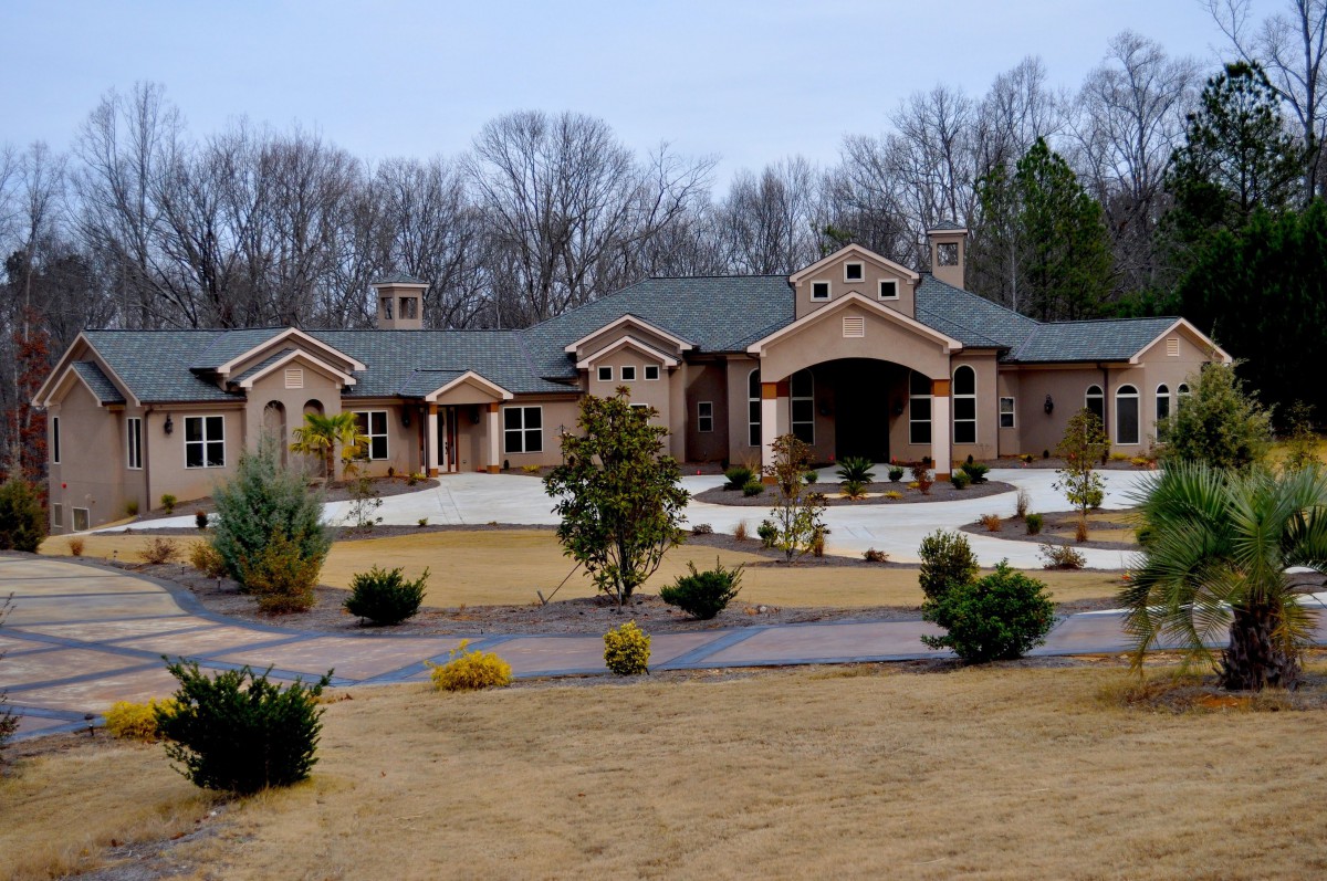 A large, modern house surrounded by a landscaped lawn and trees.