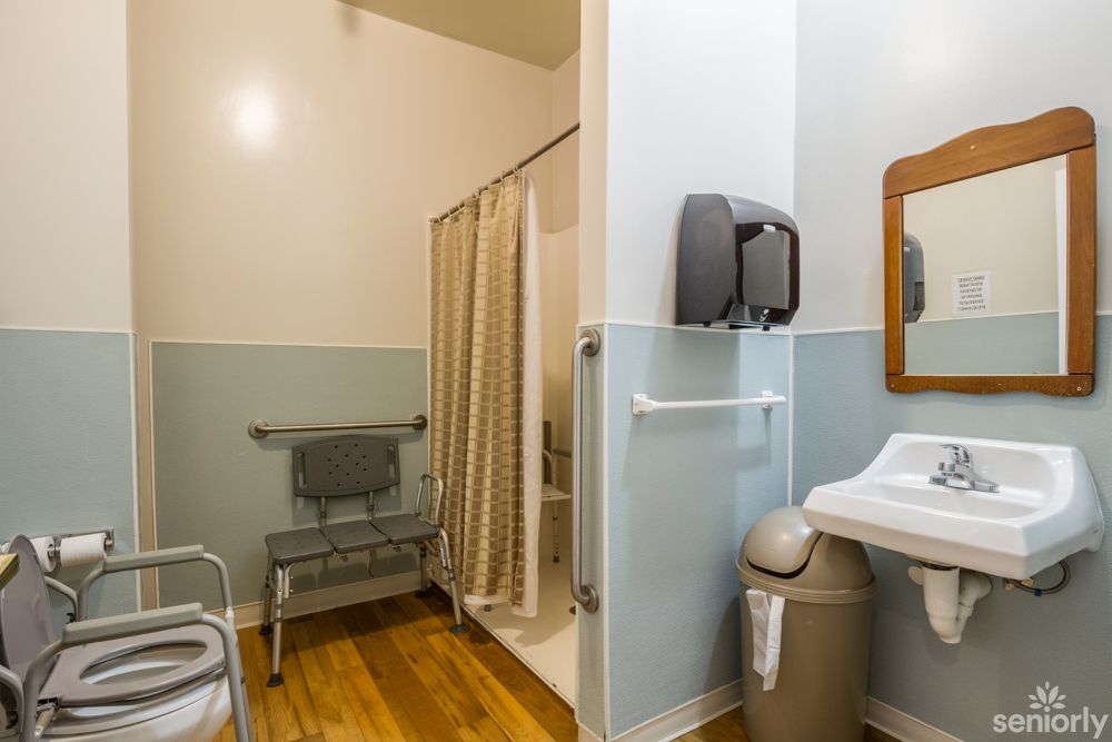 An accessible bathroom featuring a shower with grab bars, a chair, and a sink with a mirror.