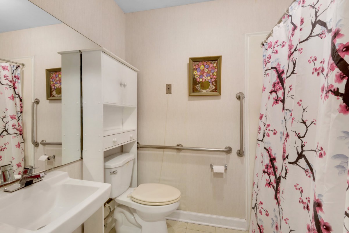 A clean and cozy bathroom with a toilet, sink, mirror, and floral shower curtain.