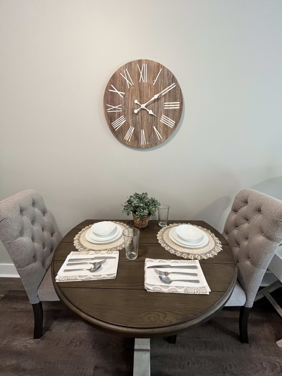 A cozy dining area featuring a small round table set for two, with elegant chairs and a decorative wall clock.