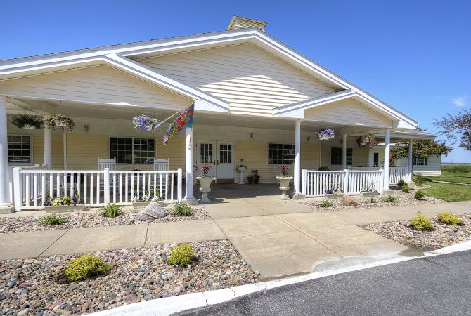 A single-story building with a large porch and colorful flags hanging, surrounded by landscaped shrubs.