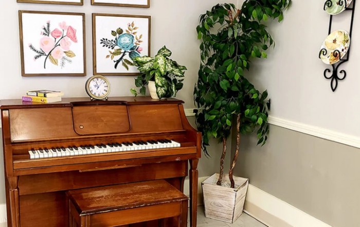 A cozy music corner with a piano, framed artwork, and lush indoor plants.