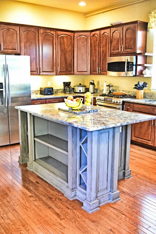 A modern kitchen with a central island featuring a granite countertop, surrounded by wooden cabinets and stainless steel appliances.