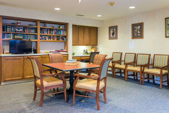 A cozy waiting room with a table and chairs, surrounded by bookshelves and decor.