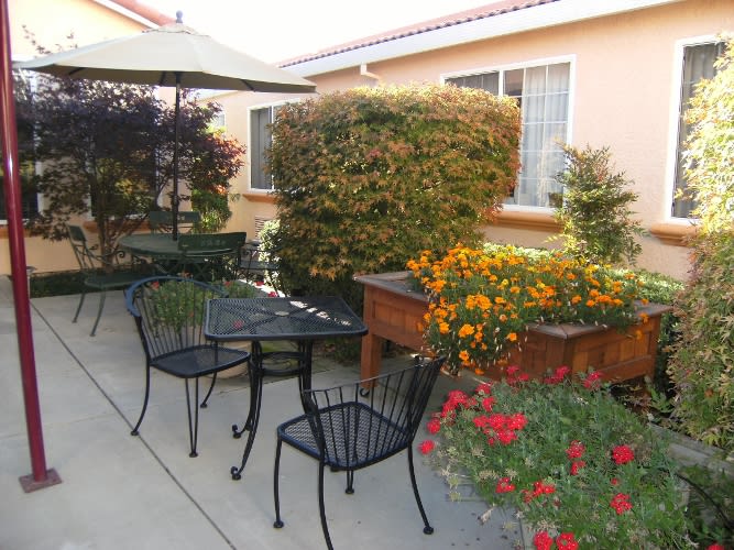 A cozy outdoor patio with a table, chairs, and vibrant flowers in the garden.