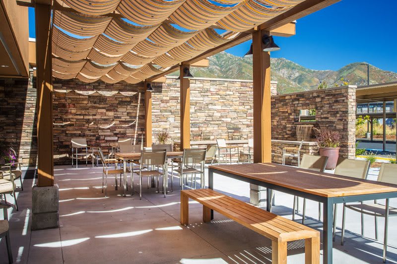 A beautiful outdoor restaurant patio with wooden furniture and a pergola, surrounded by stone walls on a sunny day.