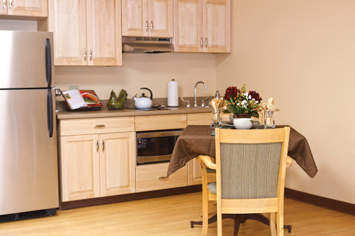 A cozy kitchen featuring light wooden cabinets, a dining table set for two, and decorative flowers.
