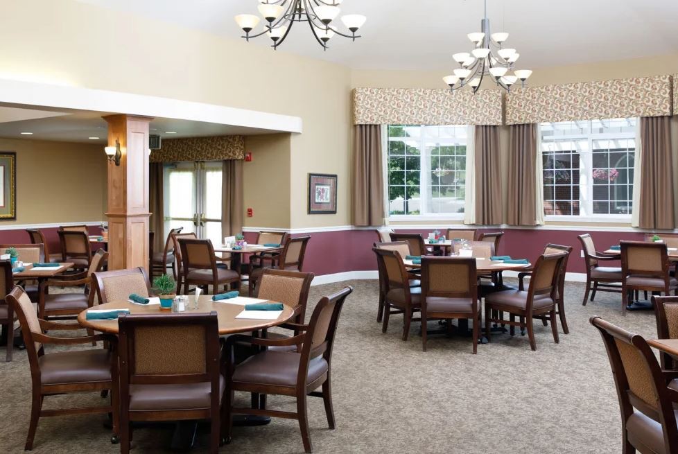 A well-lit dining room with multiple tables and chairs arranged neatly under elegant chandeliers.