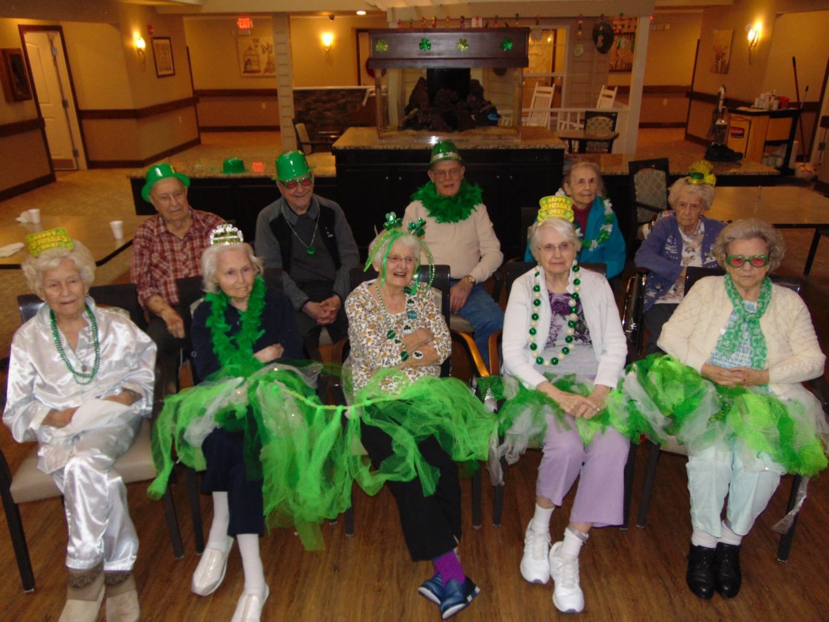 A group of seniors dressed in green costumes and hats, gathered indoors for a celebration.