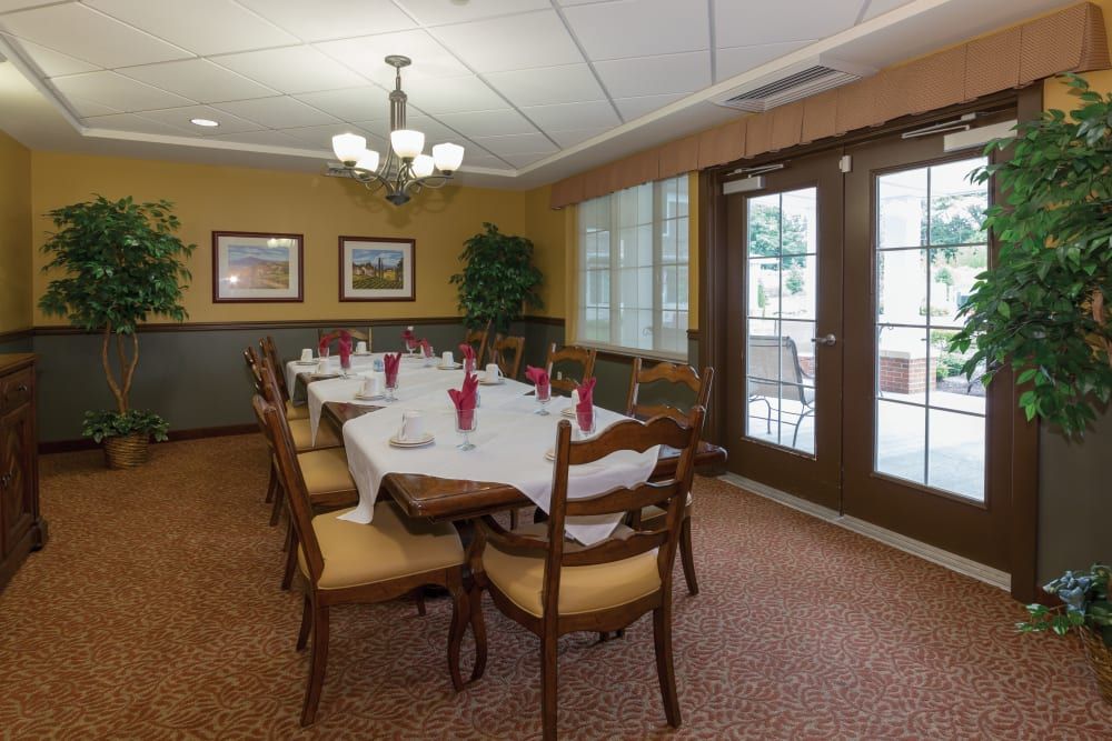 A formal dining room with a long table set for guests, featuring elegant chairs and natural lighting from large windows.