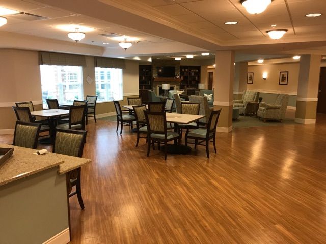 A spacious dining area with wooden floors, tables, and chairs under warm lighting.