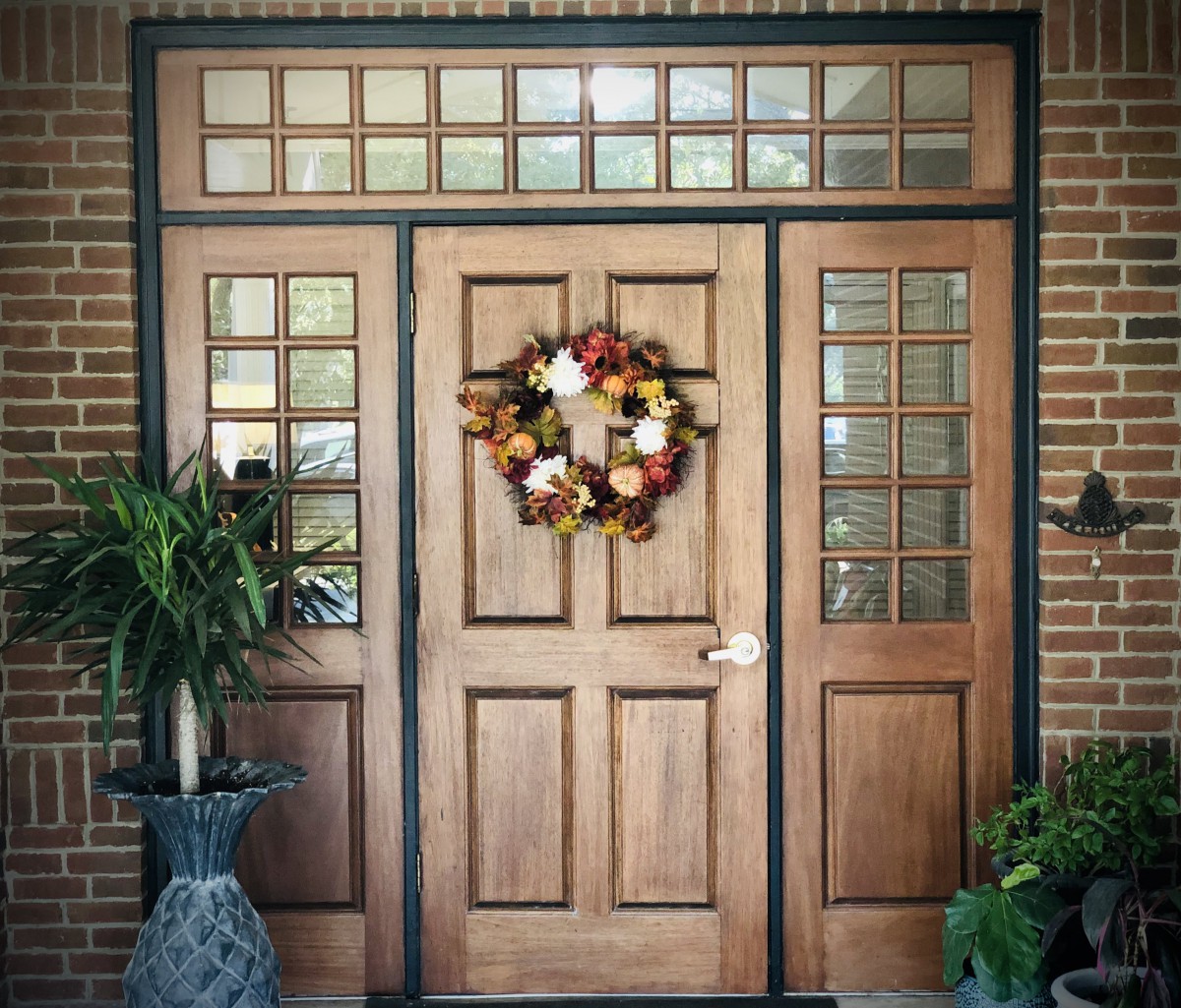 A beautiful wooden front door adorned with an autumn wreath, flanked by potted plants.