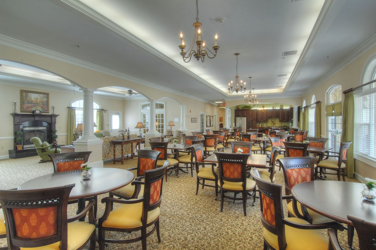 An elegant dining room with multiple tables and chairs, featuring chandeliers and a carpeted floor.