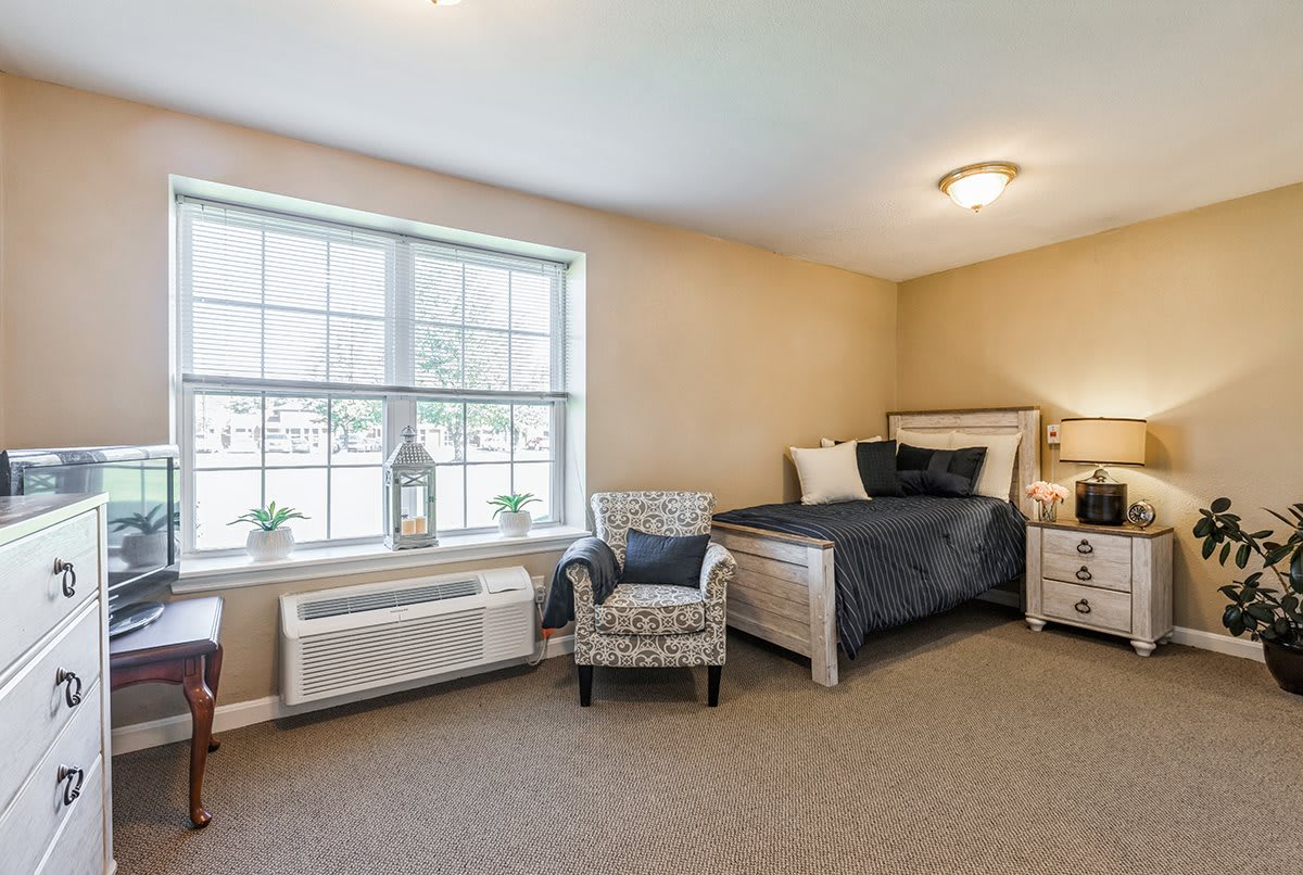 A cozy bedroom with a bed, chair, and large window allowing natural light.