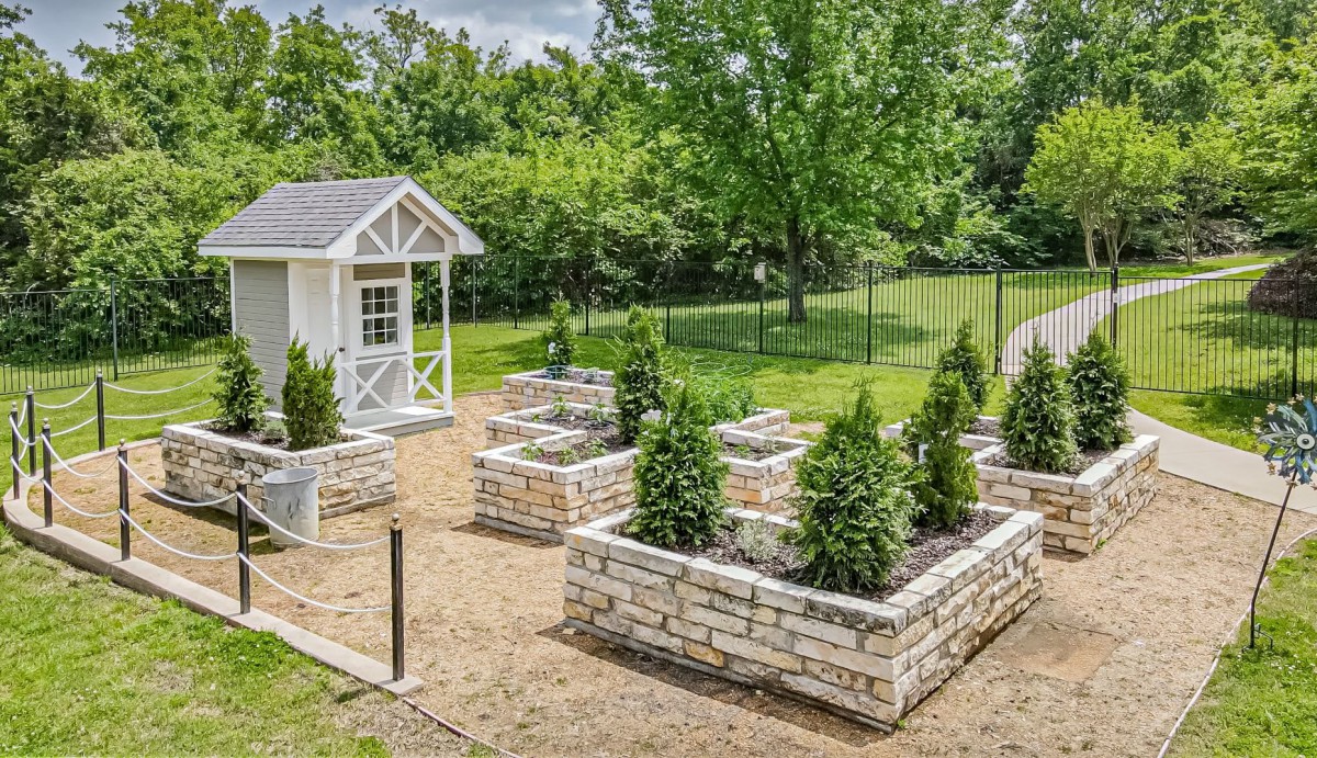 A garden with raised stone beds and a small shed, surrounded by lush greenery.