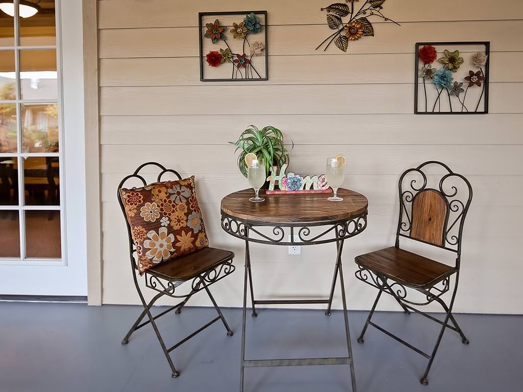 A cozy outdoor patio setup with a small round table, two decorative chairs, and wall art.